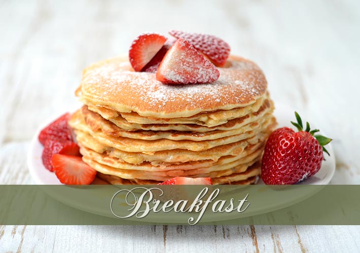A stack of pancakes topped with sliced strawberries and powdered sugar sits on a white plate, with whole and sliced strawberries around. The word “Breakfast” is written across the image in elegant script.