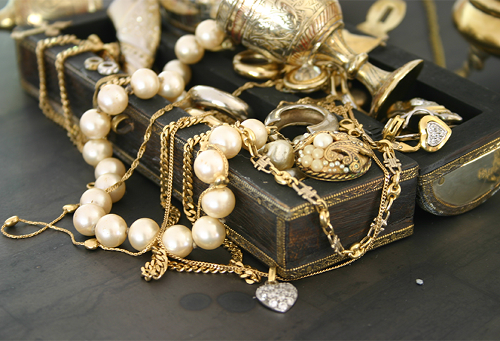 A pile of gold chains, pearl necklaces, and heart-shaped lockets is draped over an ornate black box, with decorative gold items scattered in the background—evoking the hidden treasures you might discover while exploring things to do in Springfield Ohio.