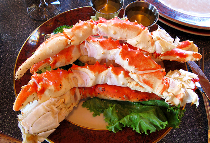 Cooked king crab legs are served on a plate with lettuce and two cups of dipping butter, ready to eat—an indulgent dish perfect to enjoy after exploring things to do in Springfield, Ohio. The crab legs are large, spiky, and reddish-orange with white meat visible.