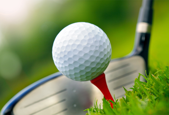 A close-up of a golf ball on a red tee, positioned in front of a golf club driver on green grass, ready to be hit—perfect for those seeking fun things to do in Springfield Ohio.